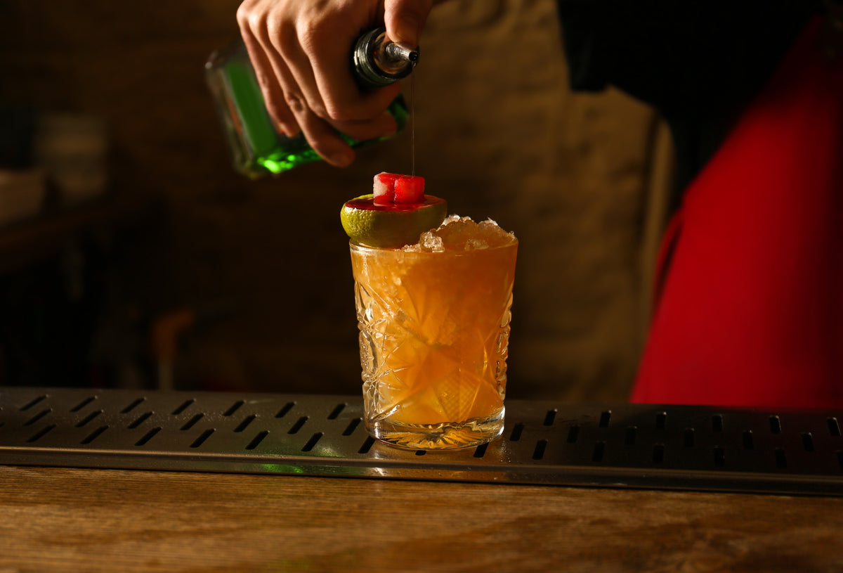Cocktail being garnished with a lime and cherry on a bar counter.