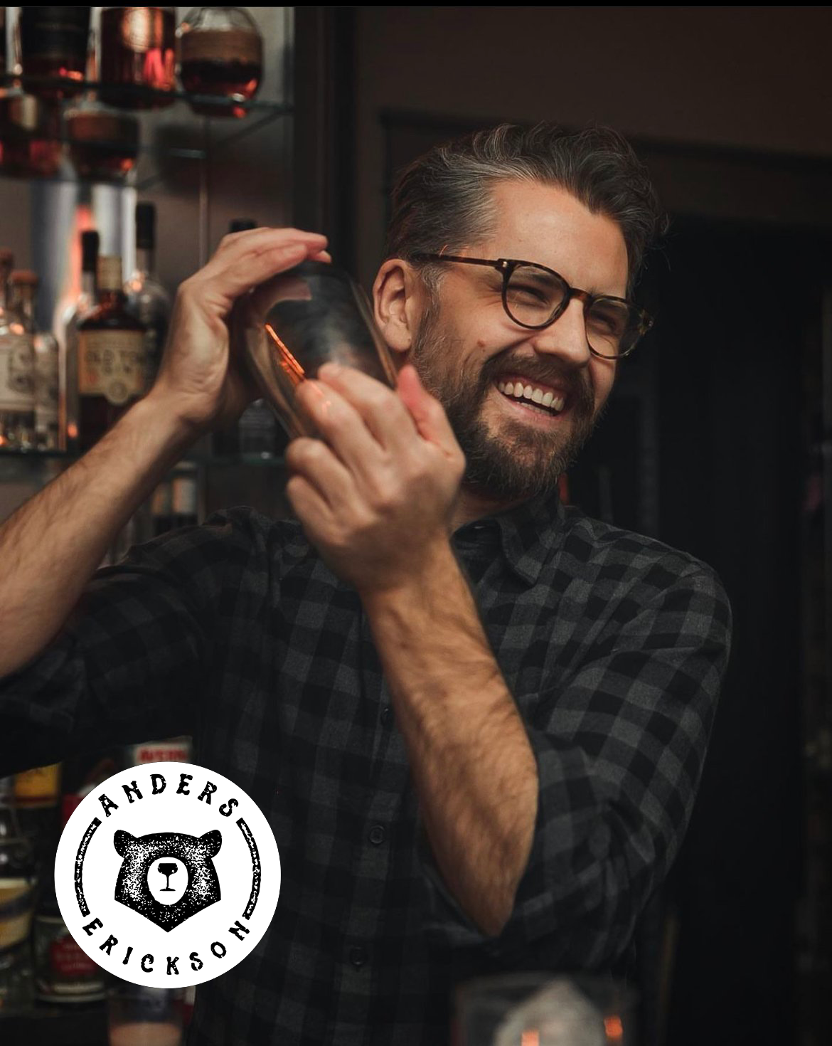 Man in a bar setting with a drink, wearing glasses and a checkered shirt, with 'Anders Erickson' logo.