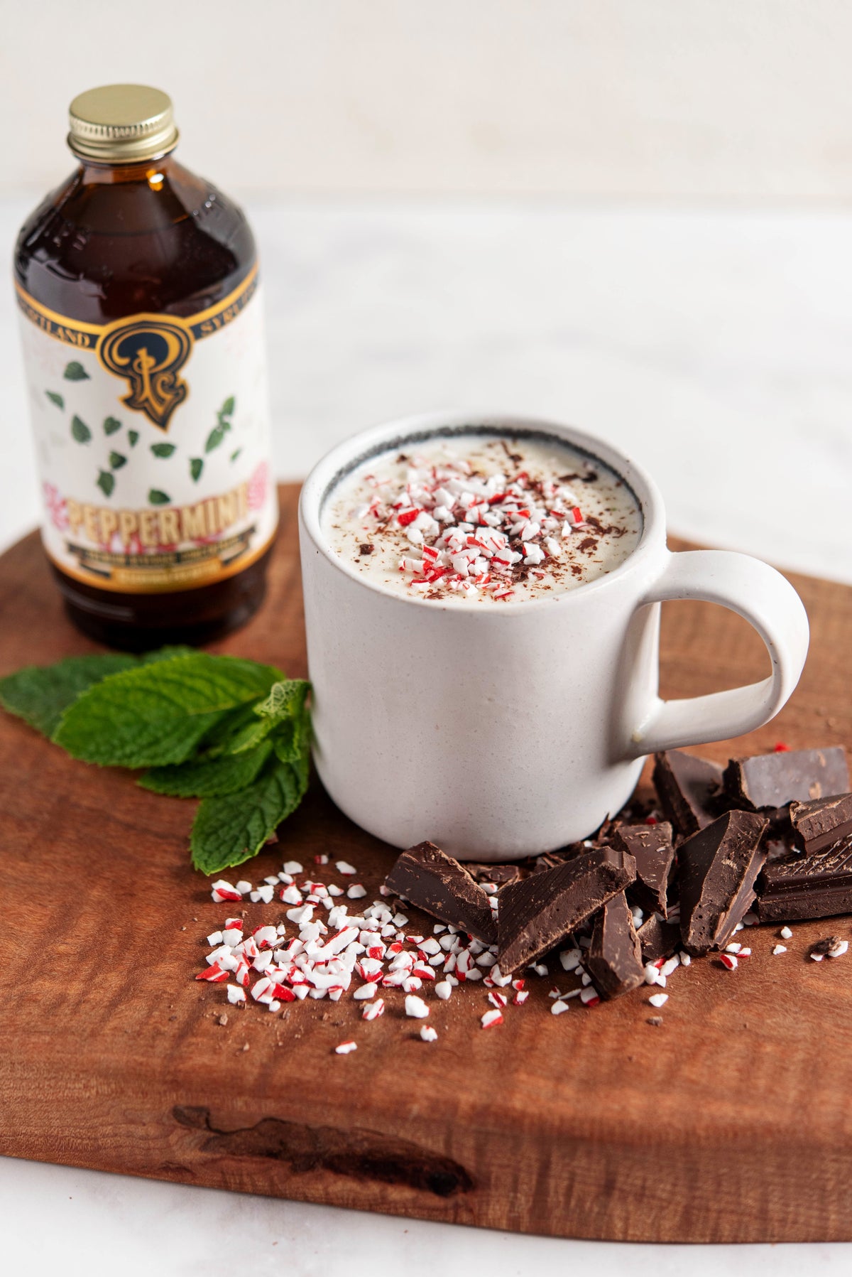 Mug of hot chocolate with peppermint and chocolate on a wooden board, next to a bottle of peppermint extract.