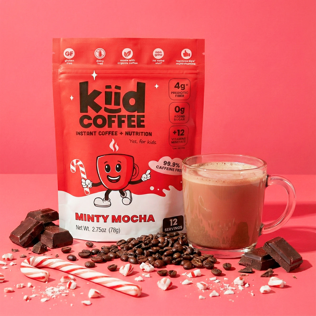 A stand-up pouch of KÜD Coffee Minty Mocha instant coffee and nutrition mix is shown on a pink studio background, with a glass mug of the prepared drink, coffee beans, candy canes, and chocolate pieces arranged around it.