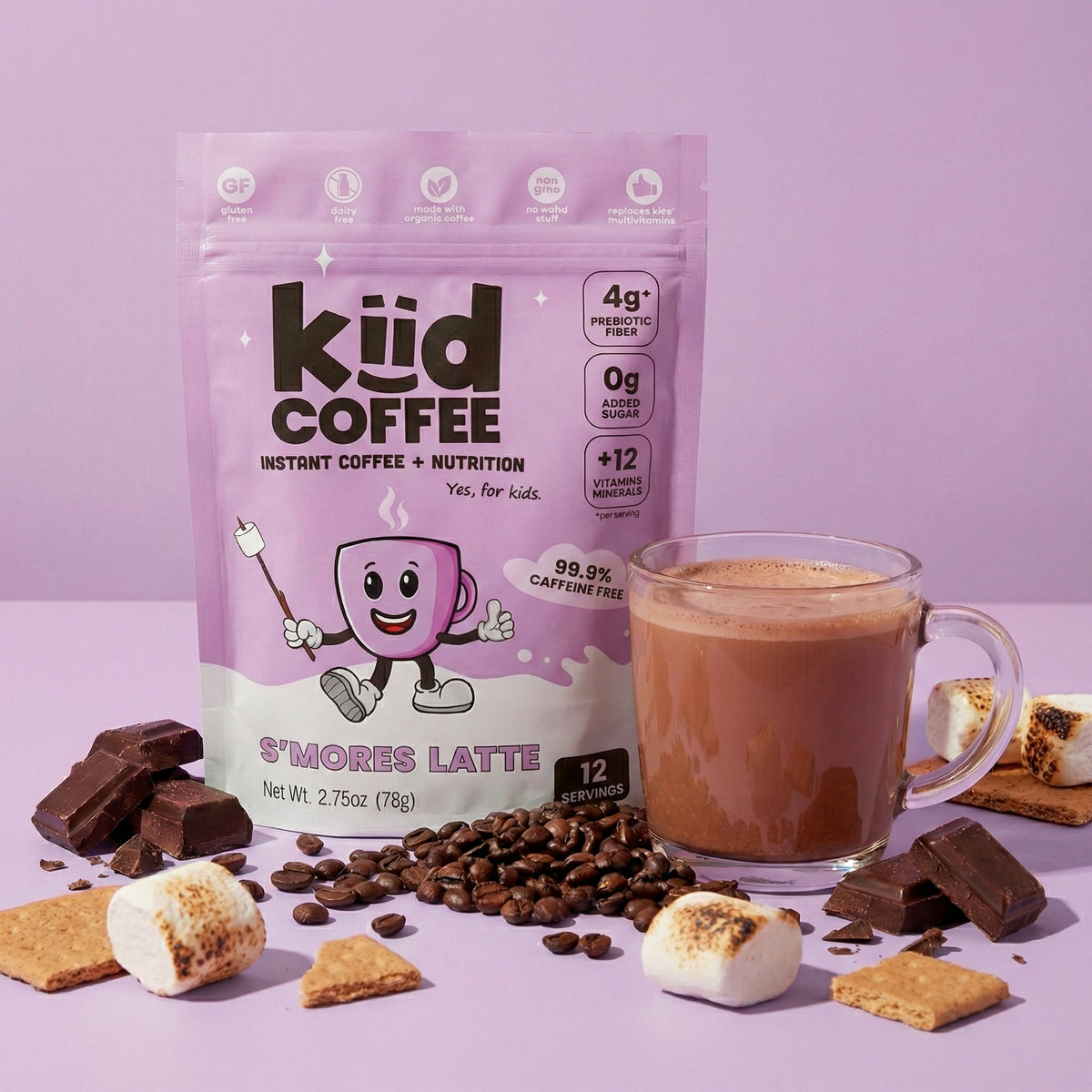 A package of KüD Coffee S'mores Latte stands on a lavender background with a glass mug of hot chocolate surrounded by marshmallows, chocolate pieces, coffee beans, and graham crackers.