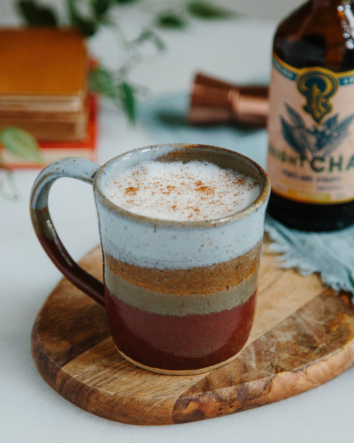 Mug of layered hot drink on a wooden coaster with a bottle of matcha in the background.