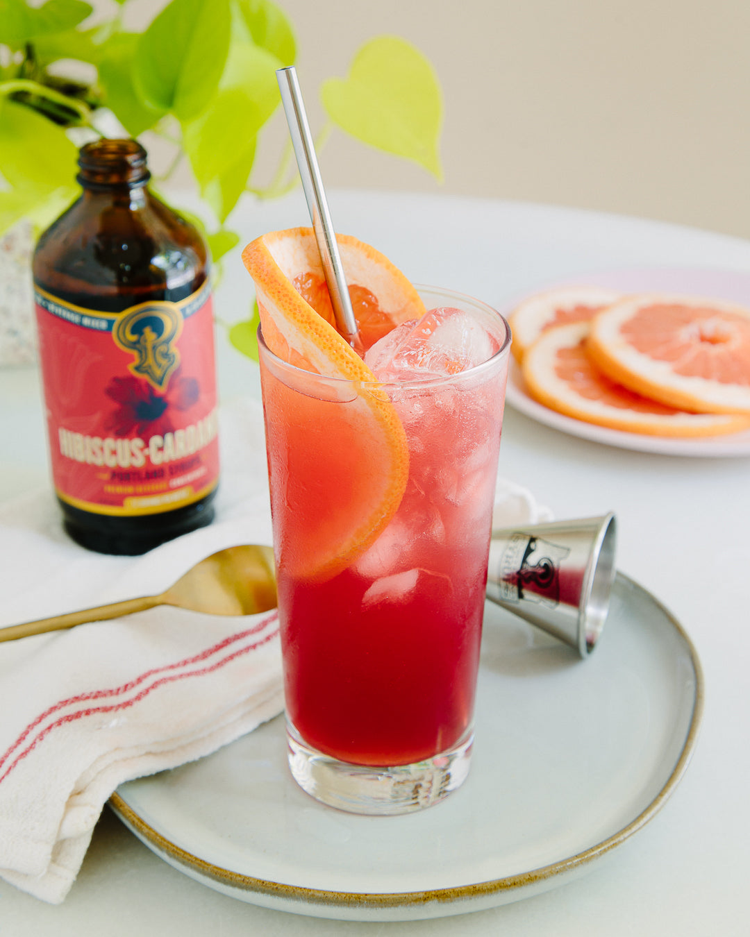 Red cocktail with orange slices in a glass on a white plate, with a bottle of Buc-ee's candy in the background.