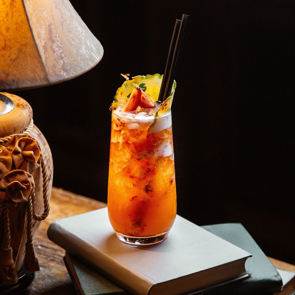 Cocktail with fruit garnish on a book with a warm light source