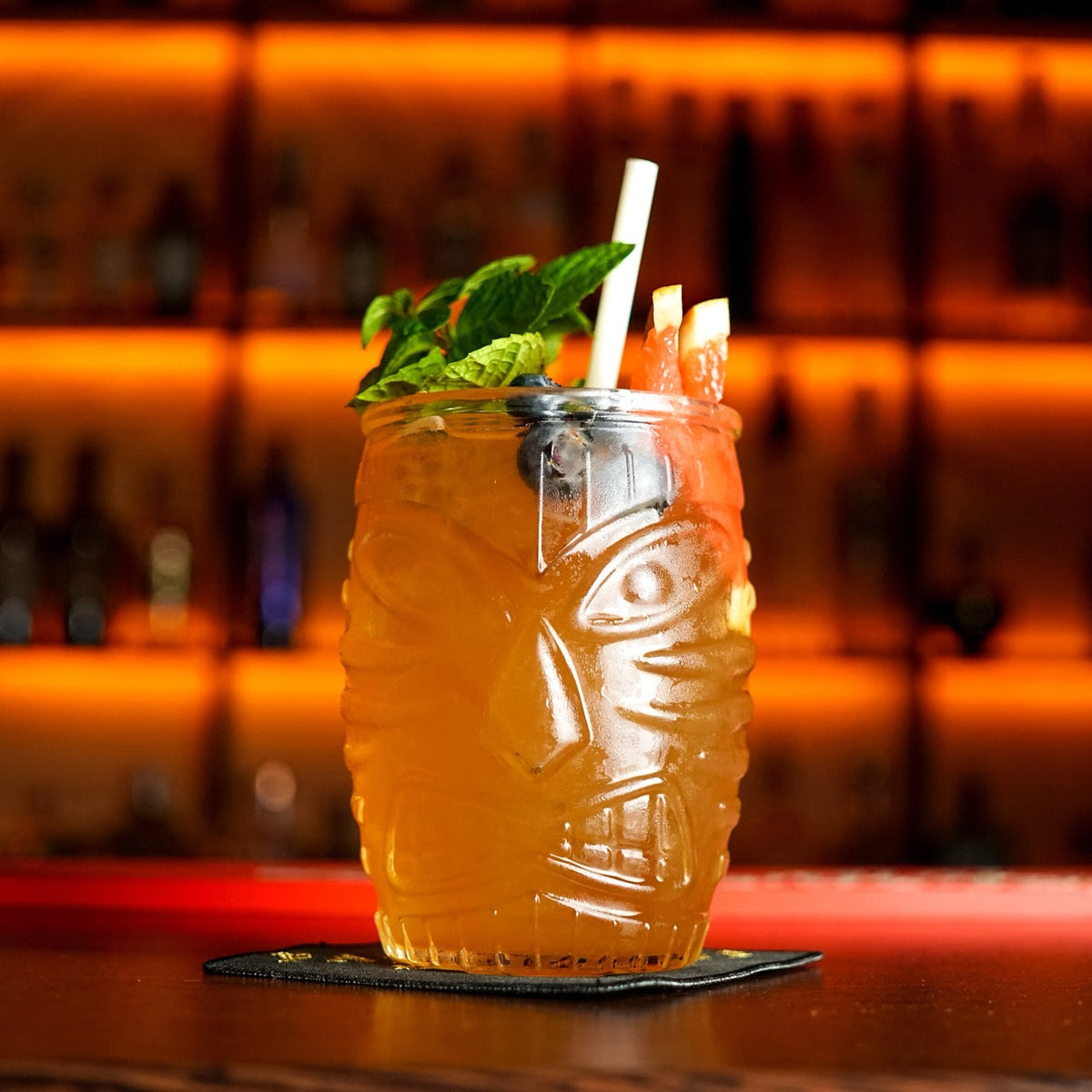 Cocktail in a tiki mug with a straw and mint leaves on a bar counter.