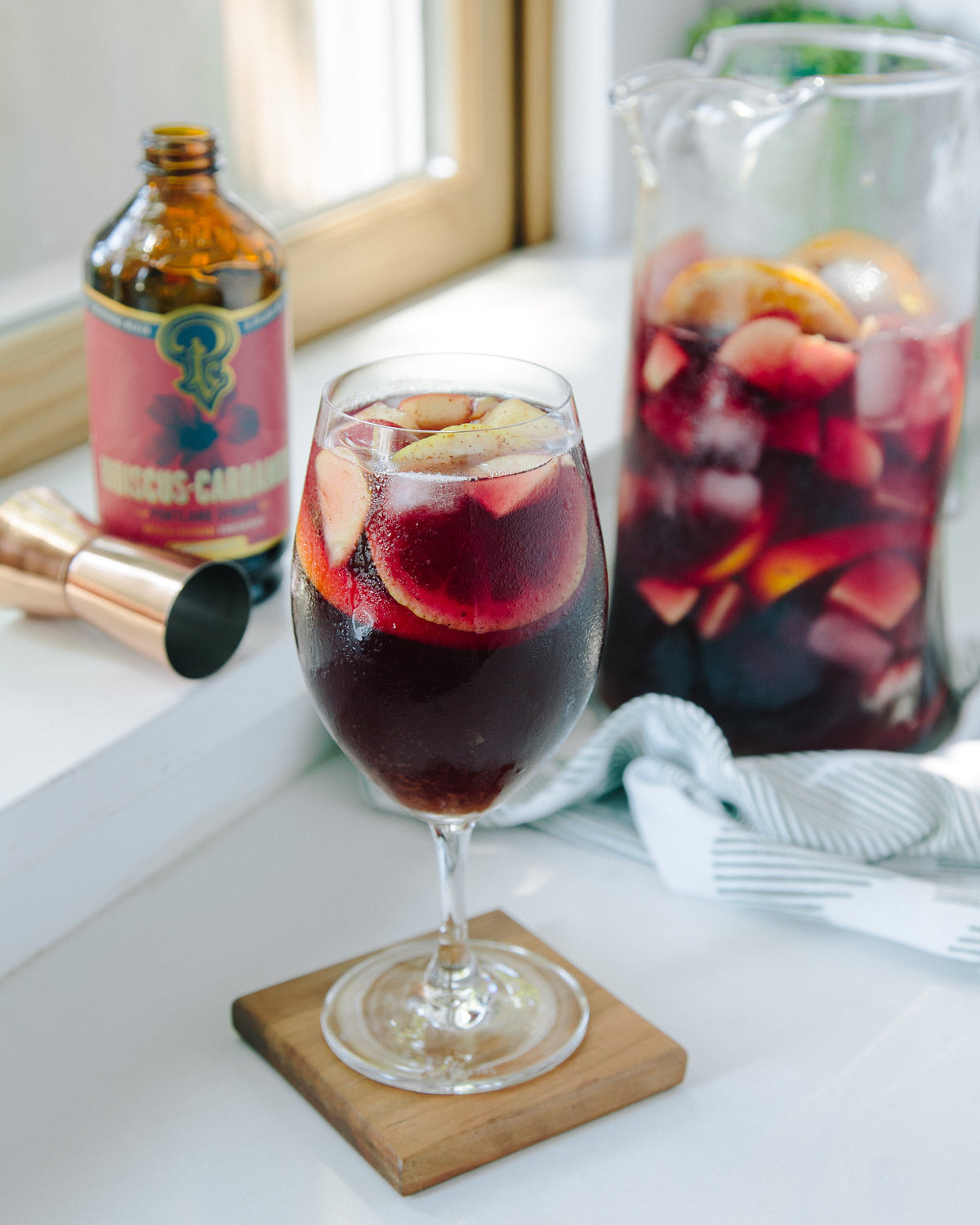 Wine glass with sangria on a coaster, with a bottle and pitcher of sangria in the background.