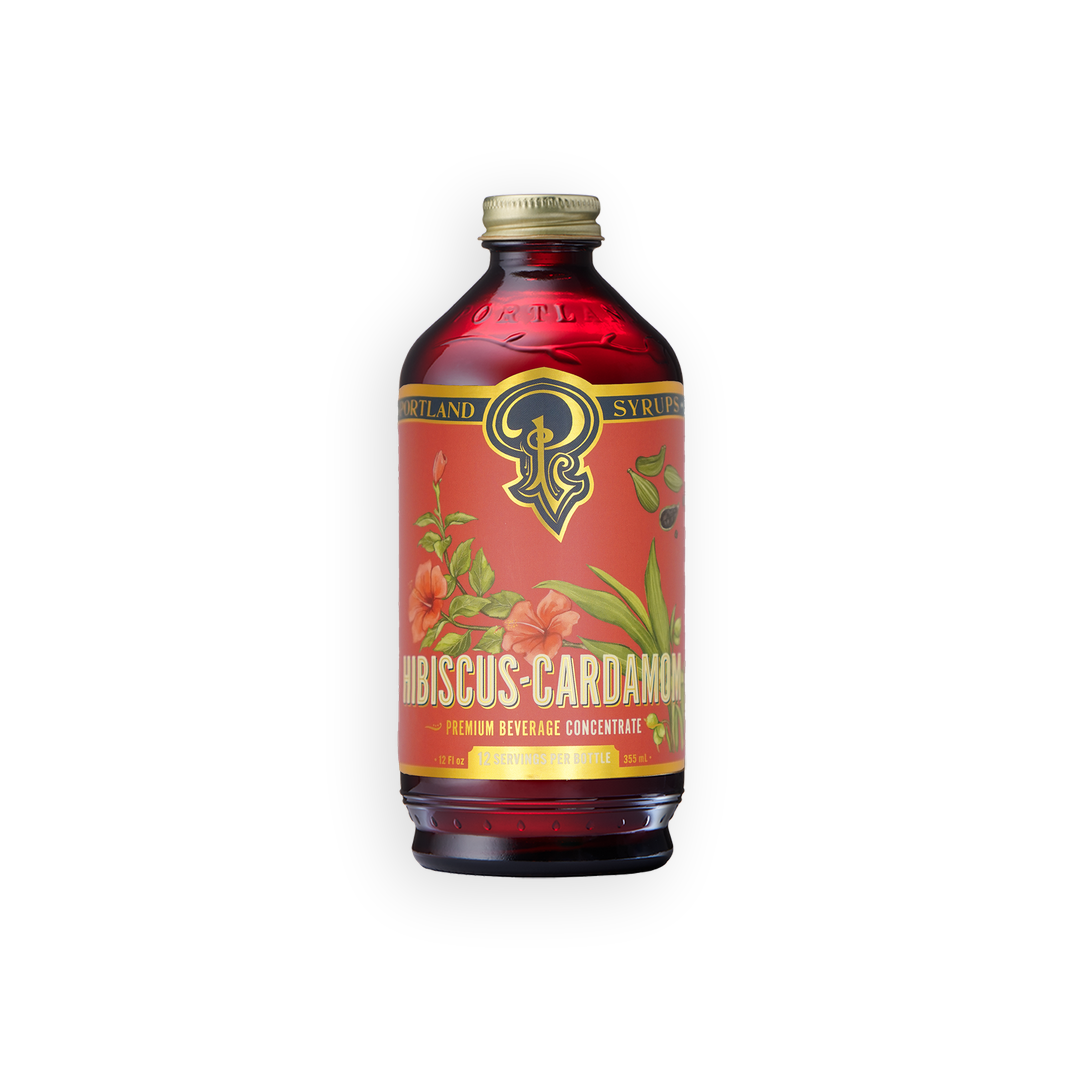 A bottle of Syrup and Syrupz Hibiscus Cardamom premium beverage concentrate, featuring a red label with floral illustrations and a gold cap, set against a plain white background.