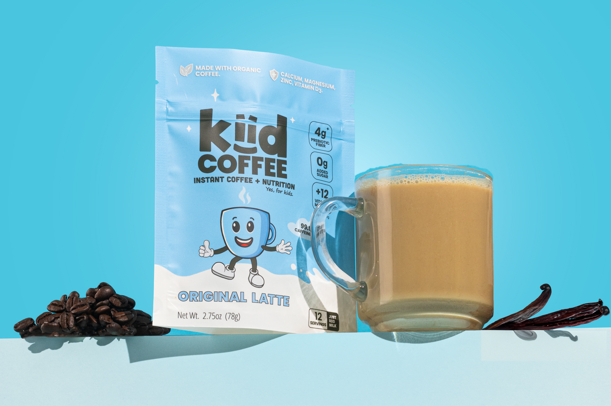 A package of kid coffee Instant Coffee + Coffee Nutrition Original Latte stands next to a glass mug filled with iced coffee, with coffee beans and vanilla beans on a light blue background.