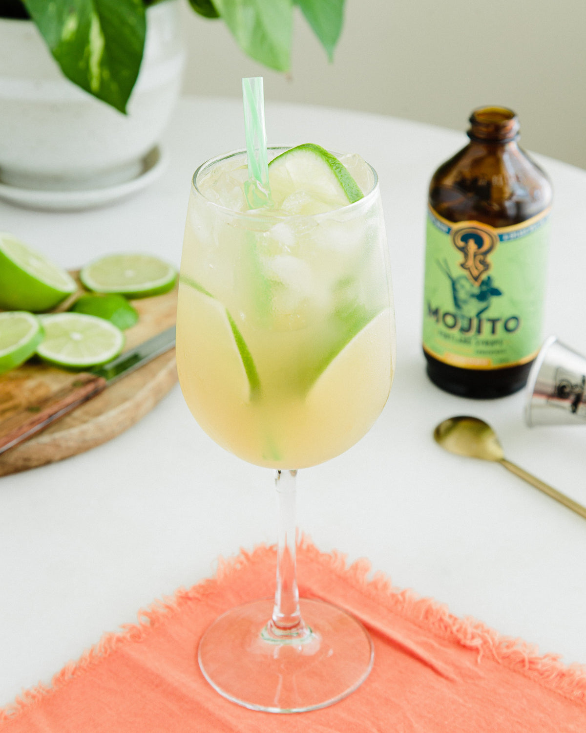 Mojito cocktail with lime slices and a bottle of Mojito on a table.