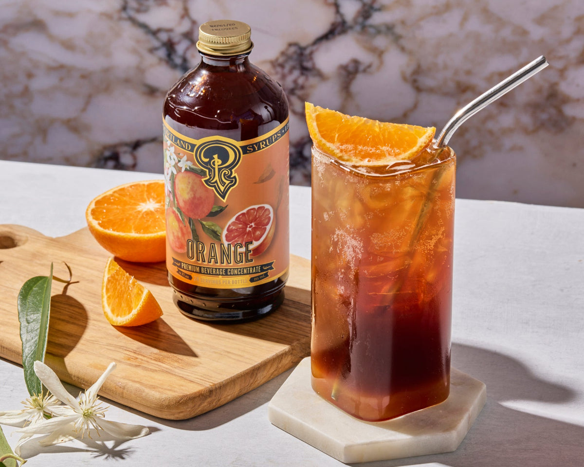 Bottle of Stoli Orange liqueur with a glass of iced tea garnished with an orange slice on a marble surface.