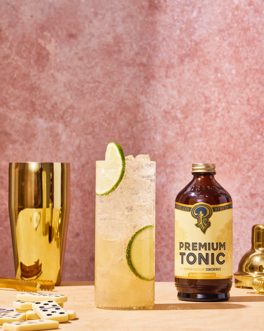 Bottle of premium tonic with a cocktail and gold glass on a pink background