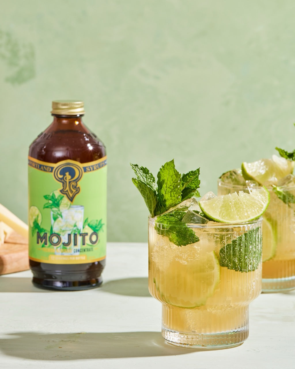 Mojito bottle with two glasses of mojito on a light green background