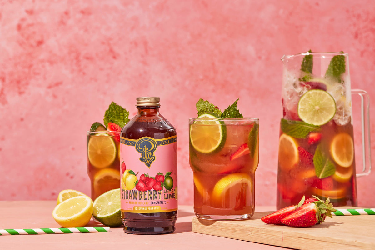 Strawberry lime iced tea with a bottle, glasses, and pitcher on a pink background