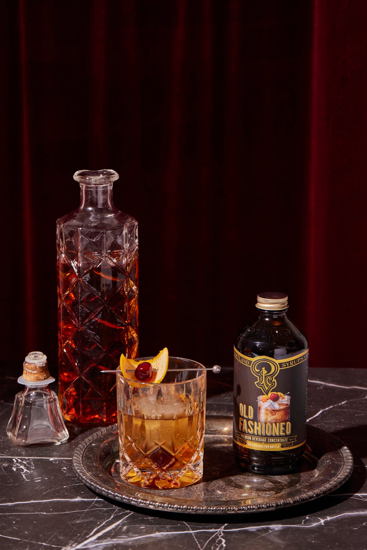 Old Fashioned cocktail with a bottle of Old Fashioned on a dark surface