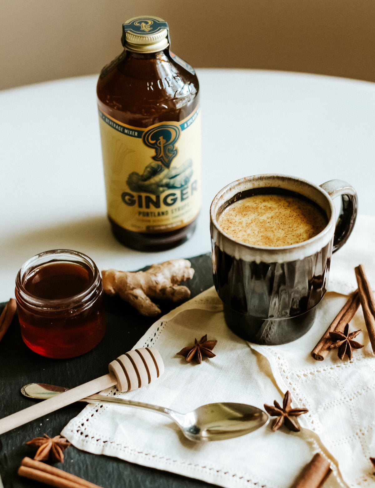 Ginger ale bottle, mug with ginger drink, and spices on a table.