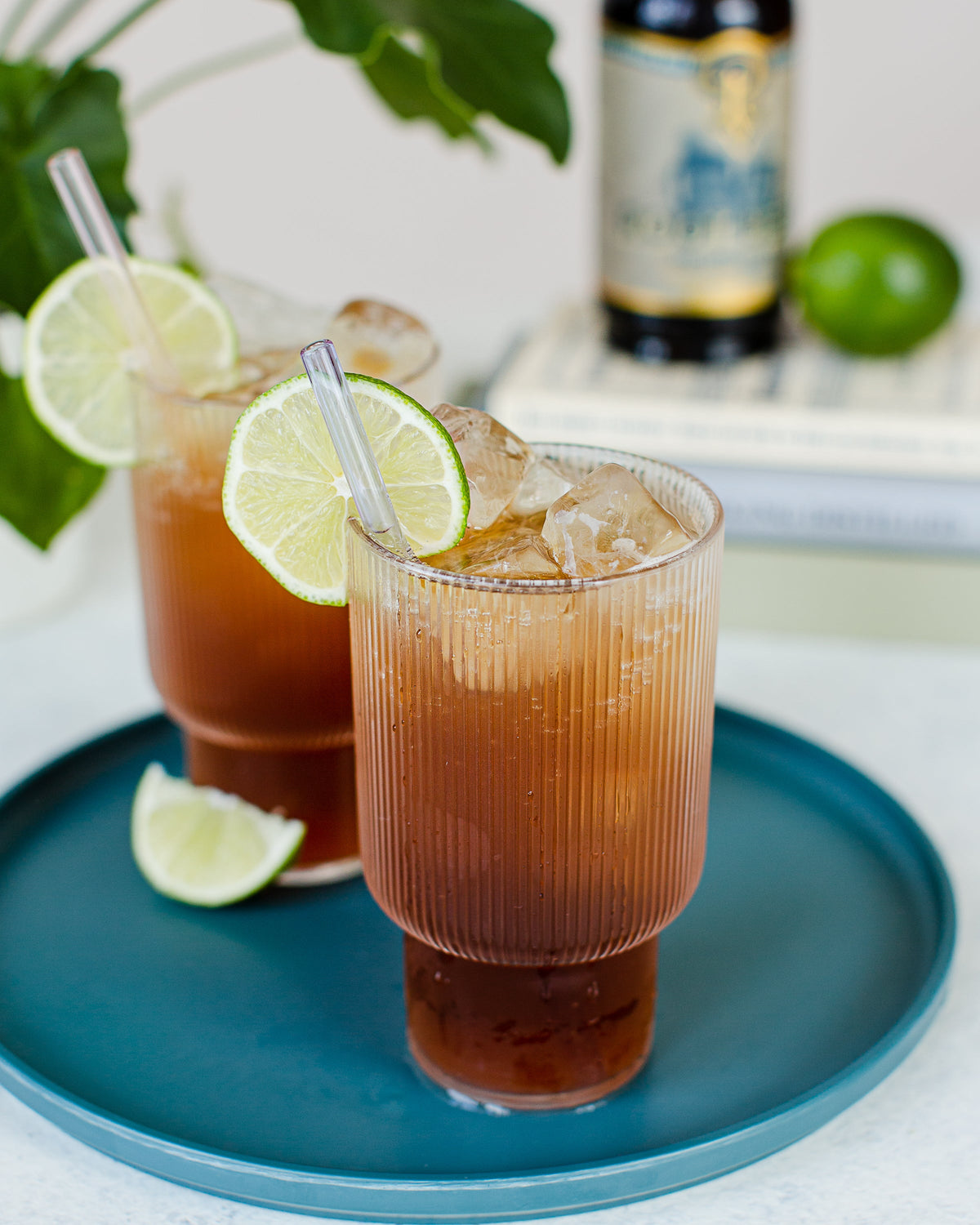 Two glasses of iced tea with lime slices on a blue plate, with a bottle in the background.