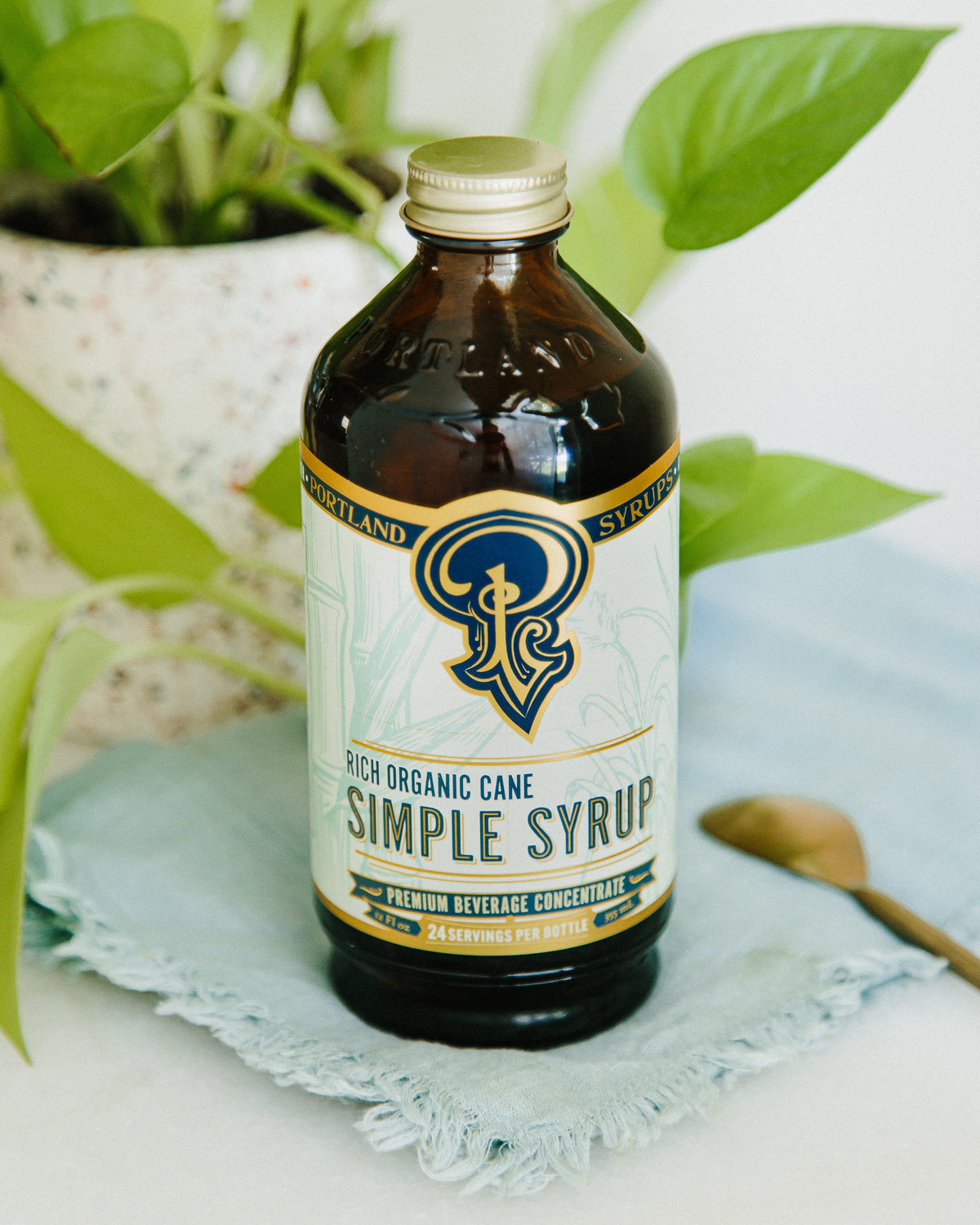Bottle of Portland Stripes Simple Syrup on a white surface with green leaves in the background