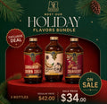 Three bottles of holiday-flavored syrup from Sacred Syrup House displayed on a red pedestal against a dark green holiday-themed background with pine branches and a pinecone. The bottles are labeled Cinnamon Brown Sugar, Bright Charms, and Spiced Cranberry.